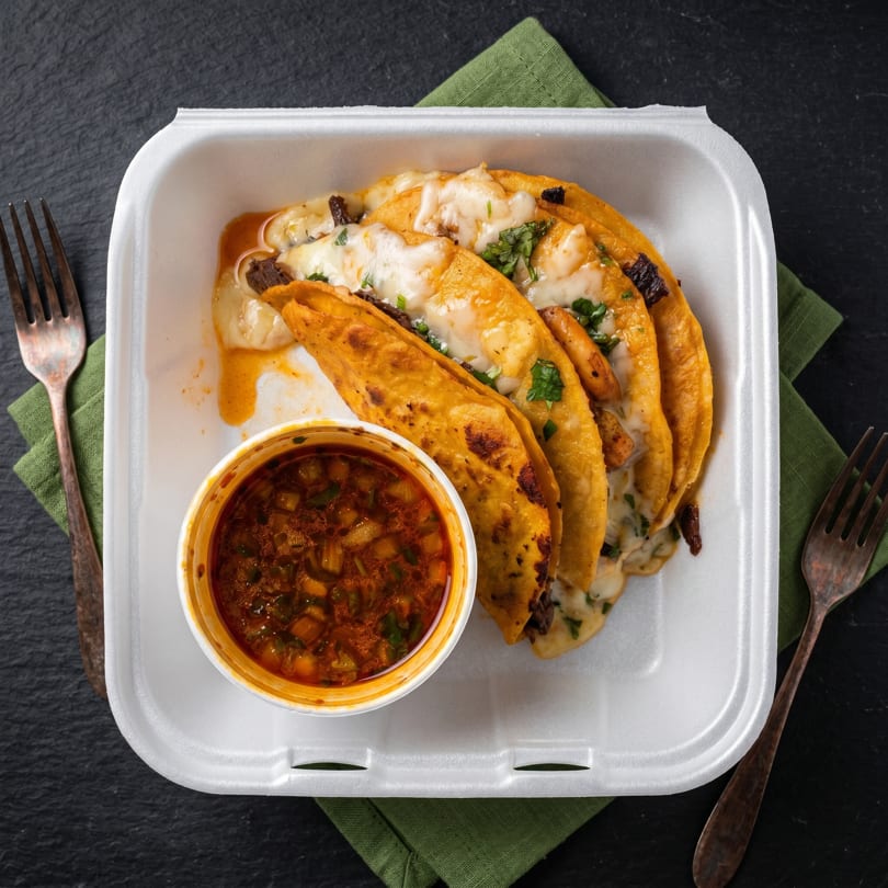 Four cheesy birria tacos with cilantro and a side of consommé in a white takeout container.